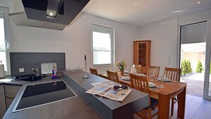 A modern kitchen with a central island, dining area with wooden chairs, and a view of the outdoors. - 2-story vacation home, quiet location, about 1.3 kilometers from the sandy beach (Baltic Sea) (Glowe)