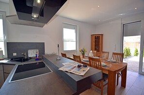A modern kitchen with a central island, dining area with wooden chairs, and a view of the outdoors. - 2-story vacation home, quiet location, about 1.3 kilometers from the sandy beach (Baltic Sea) (Glowe)