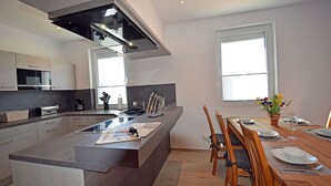 A modern kitchen with a central island, dining area with wooden chairs, and large windows providing natural light. - 2-story vacation home, quiet location, about 1.3 kilometers from the sandy beach (Baltic Sea) (Glowe)