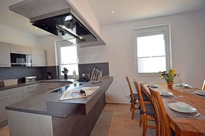 A modern kitchen with a central island, dining area with wooden chairs, and large windows providing natural light. - 2-story vacation home, quiet location, about 1.3 kilometers from the sandy beach (Baltic Sea) (Glowe)