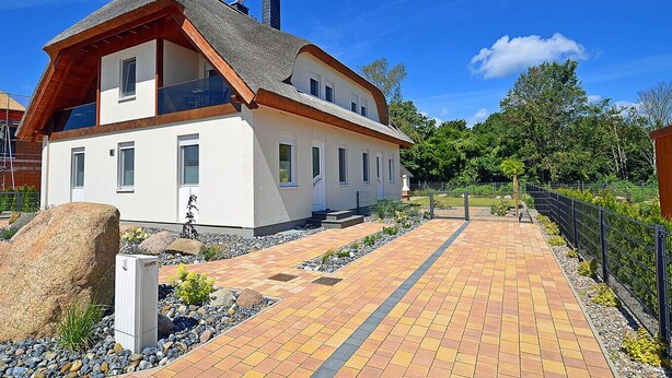 A two-story house with a sloped roof, a paved pathway leading to the entrance, and a fenced garden area. - 2-story vacation home, quiet location, about 1.3 kilometers from the sandy beach (Baltic Sea) (Glowe)