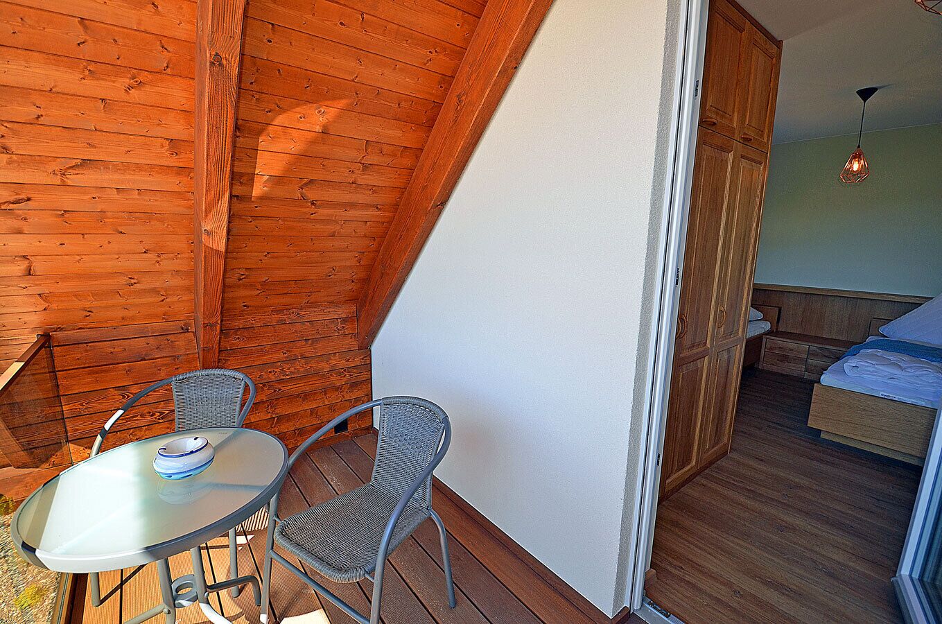 Ein kleines Zimmer mit Holzbalkendecke, einem Bett, einem Tisch mit Stühlen und einer hängenden Lampe.