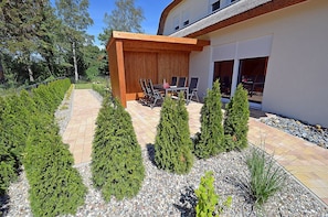 A modern outdoor patio with a wooden pergola, seating, and neatly trimmed shrubs. - 2-story vacation home, quiet location, about 1.3 kilometers from the sandy beach (Baltic Sea) (Glowe)