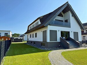 Ein modernes, zweistöckiges Haus mit Satteldach, Hauseingang mit Stufen und einer gepflasterten Auffahrt.