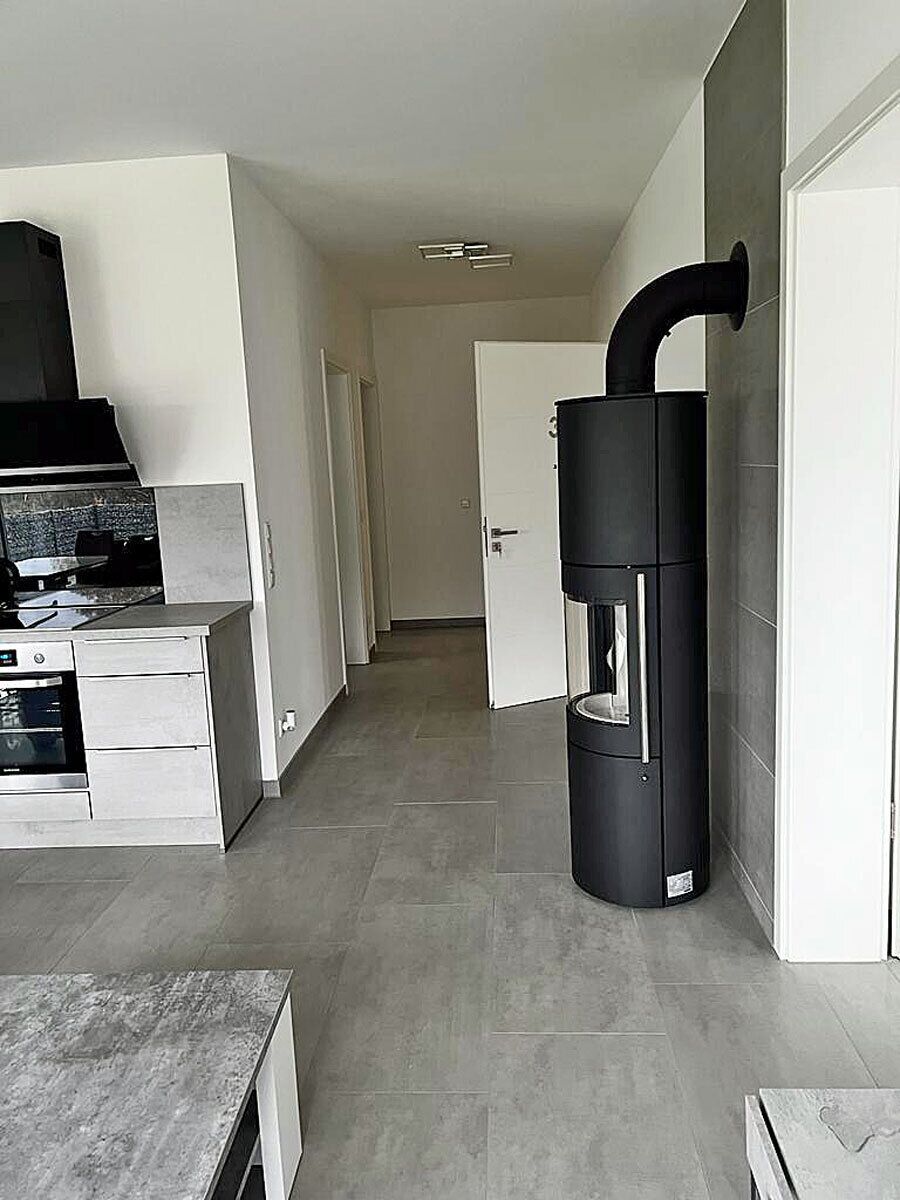 A modern kitchen with a built-in oven and a black vertical appliance, possibly a water heater, in a hallway with a door leading to another room.