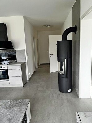 Eine moderne Küche mit Einbauofen und einem schwarzen, vertikalen Gerät, möglicherweise einem Durchlauferhitzer, in einem Flur mit einer Tür zu einem anderen Raum.