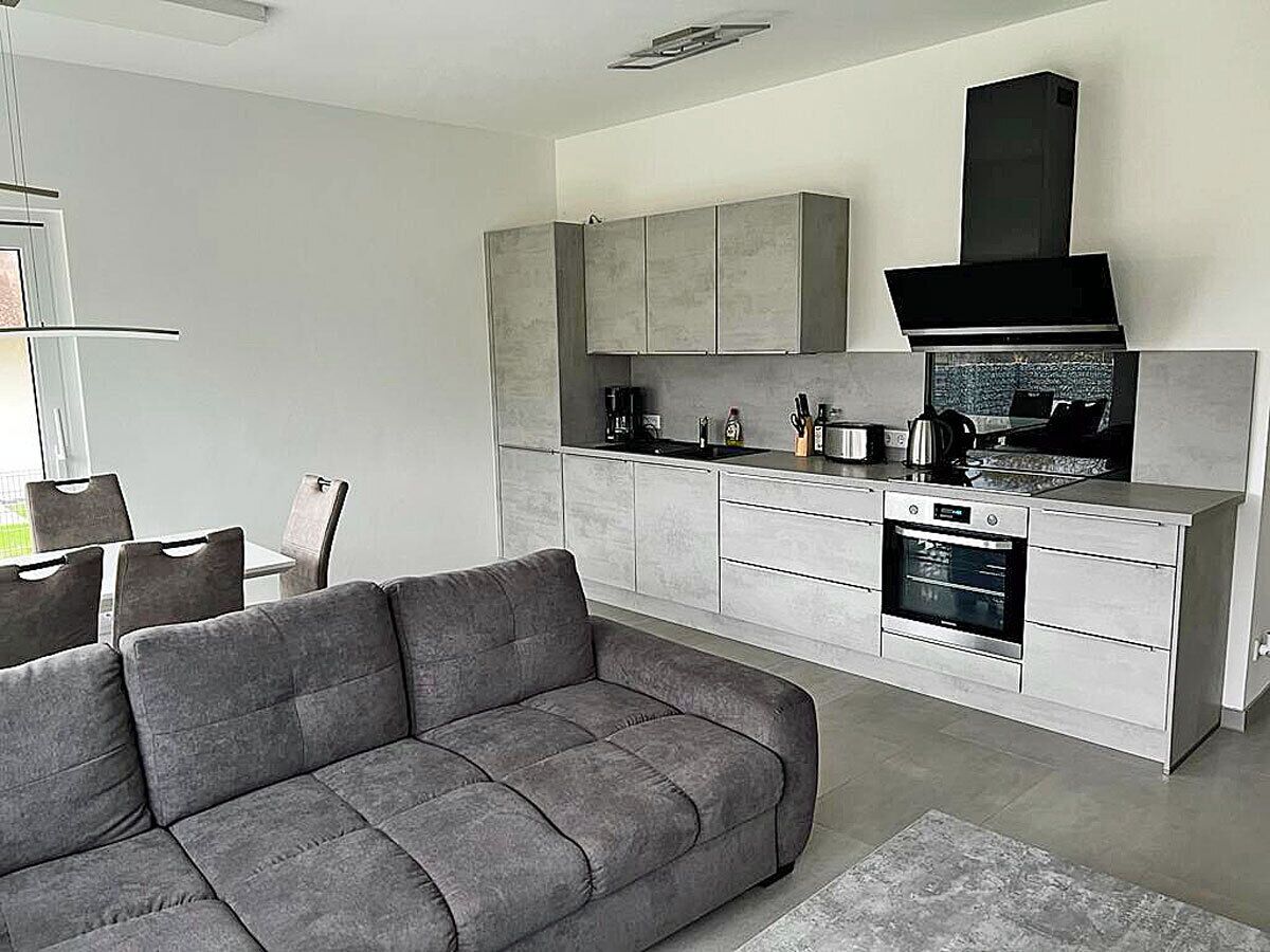 A modern kitchen with grey cabinets, a built-in oven, and a black range hood.