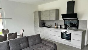 A modern kitchen with grey cabinets, a built-in oven, and a black range hood. - Modern vacation rental with a fireplace, about 1,300 meters from the sandy beach, 3 bedrooms, sleeps up to 6 people (Glowe)