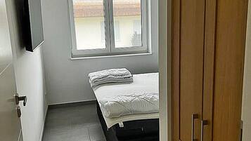 A bedroom with a bed, a window, a wardrobe, and a television on the wall.