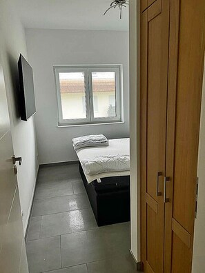 A bedroom with a bed, a window, a wardrobe, and a television on the wall. - Modern vacation rental with a fireplace, about 1,300 meters from the sandy beach, 3 bedrooms, sleeps up to 6 people (Glowe)