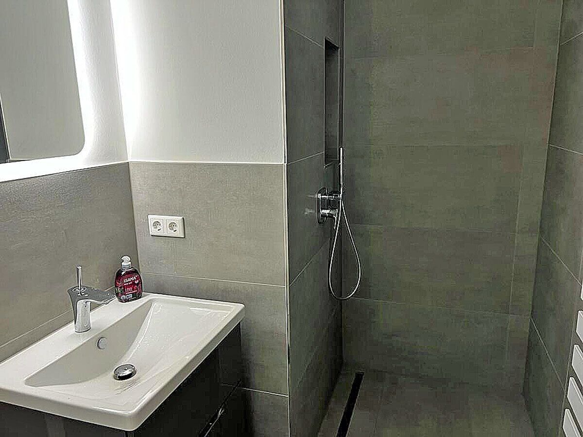 Ein Badezimmer mit einem weißen Waschbecken, einer Handbrause und einer Flasche Flüssigseife.