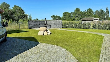 Un área pavimentada con un sendero de piedra que conduce a un césped, un muro de piedra y un vehículo estacionado a la izquierda.