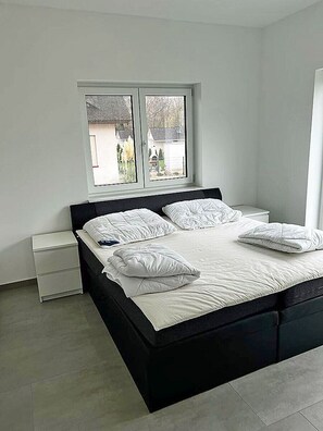 A bedroom with a bed, a window, a nightstand, and a bedside table. - Modern vacation rental with a fireplace, about 1,300 meters from the sandy beach, 3 bedrooms, sleeps up to 6 people (Glowe)