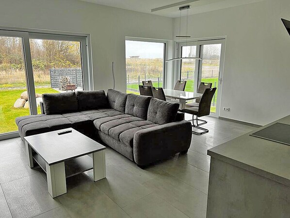 Een moderne woonkamer met een hoekbank, een eettafel met stoelen en een keuken.