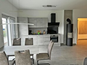 A modern kitchen with a central island, built-in appliances, and a dining area with chairs. - Modern vacation rental with a fireplace, about 1,300 meters from the sandy beach, 2 bedrooms, sleeps up to 5 people (Glowe)
