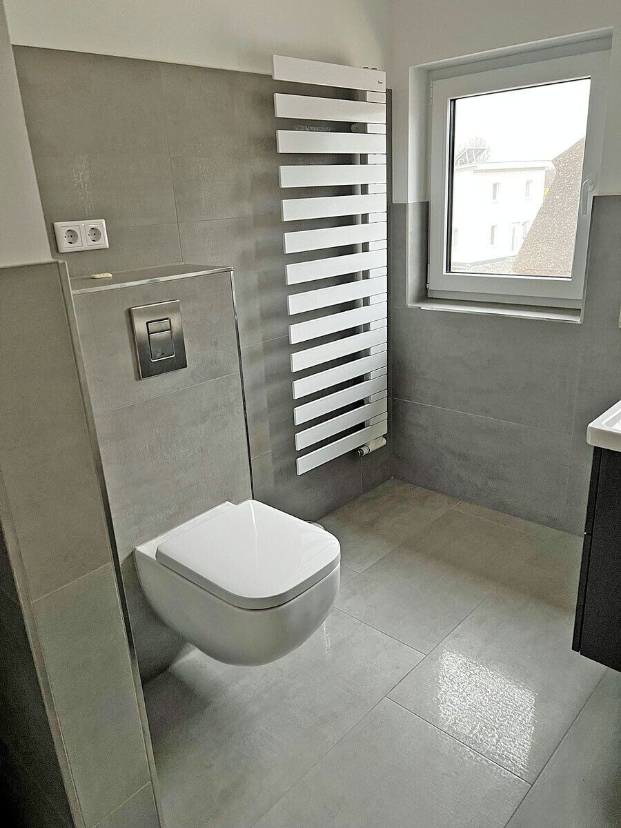 Ein Badezimmer mit Toilette, einem weißen Heizkörper und einem Fenster.