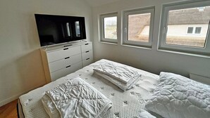 A bedroom with a bed, a TV on a dresser, and windows. - Modern vacation rental with a fireplace, about 1,300 meters from the sandy beach, 3 bedrooms, sleeps up to 6 people (Glowe)
