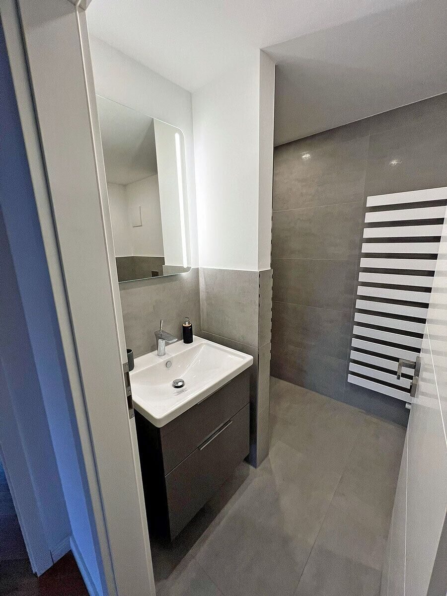 A modern bathroom with a white sink, mirror, and towel rack.