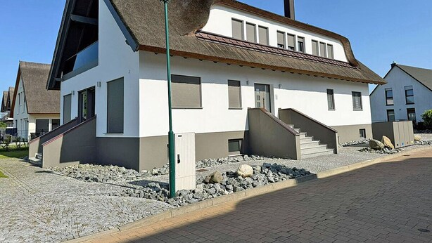 A two-story building with a steeply pitched roof, a visible chimney, and a small set of stairs leading to the entrance. - Modern vacation rental with a fireplace, about 1,300 meters from the sandy beach, 3 bedrooms, sleeps up to 6 people (Glowe)