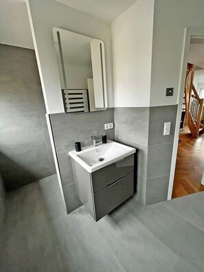 A modern bathroom with a white sink, dark cabinetry, and a large mirror. - Modern vacation rental with a fireplace, about 1,300 meters from the sandy beach, 3 bedrooms, sleeps up to 6 people (Glowe)