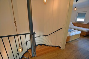 Eine Treppe mit Metallgeländer, Holzstufen und einem Bett im angrenzenden Zimmer.