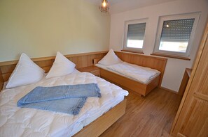 Una camera da letto con un letto grande, un letto più piccolo, due finestre con persiane e un pavimento in legno.