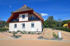 Una casa a due piani con tetto spiovente, un balcone al piano superiore e un vialetto lastricato con aiuole.