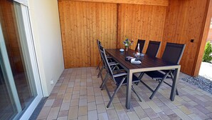 An outdoor patio with a wooden table and chairs, a vase with flowers, and a bottle. - 2-story vacation home, quiet location, about 1.3 kilometers from the sandy beach (Baltic Sea) (Glowe)