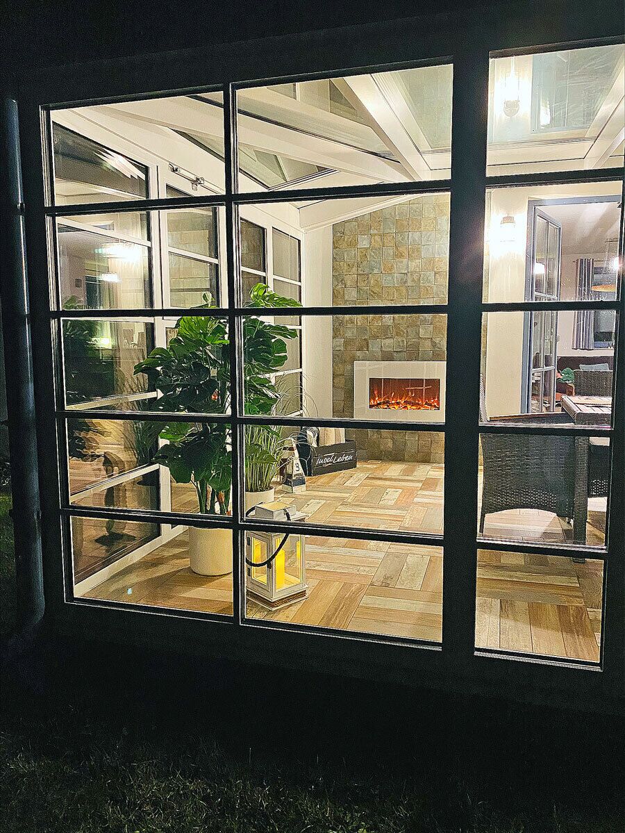 A room with a fireplace, potted plants, and a view through a window.