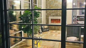 A room with a fireplace, potted plants, and a view through a window.
