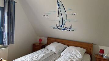 A bedroom with a single bed, two bedside tables, a window with curtains, and a wall mural of a sailboat.