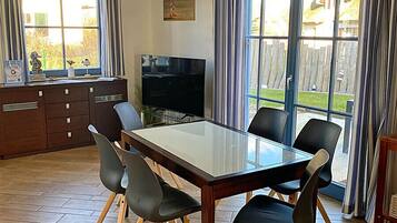A dining area with a glass table, six chairs, a television, and a kitchen counter.