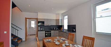 A modern kitchen with grey cabinets, a dining area with a wooden table set for four, and a staircase leading to an upper floor.