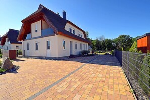 Una casa moderna de dos pisos con entrada pavimentada y jardín cercado.