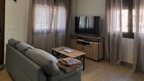 Ein Wohnzimmer mit einer Couch, einem Fernseher auf einem Holzboden, einem kleinen Tisch und Vorhängen.