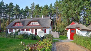 Een traditioneel huis met rieten dak, een rode deur en een tuin vol kleurrijke planten.