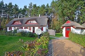 A traditional house with a thatched roof, a red door, and a garden with colorful plants. - Half of a vacation home with a fireplace and sauna, right next to the forest, about 500 meters from the sandy beach (Glowe)