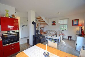 A modern living room with a red kitchen, a staircase, and a dining area. - Half of a vacation home with a fireplace and sauna, right next to the forest, about 500 meters from the sandy beach (Glowe)