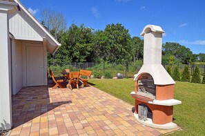Um pátio com piso de tijolos, churrasqueira e mobiliário de madeira.