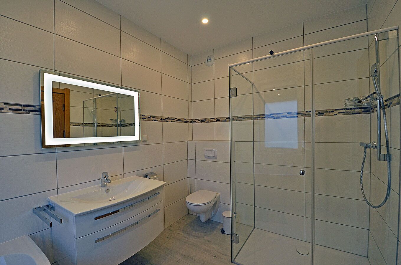 Ein modernes Badezimmer mit einer gläsernen Duschkabine, einem weißen Waschbecken mit Spiegel darüber und einer Toilette.
