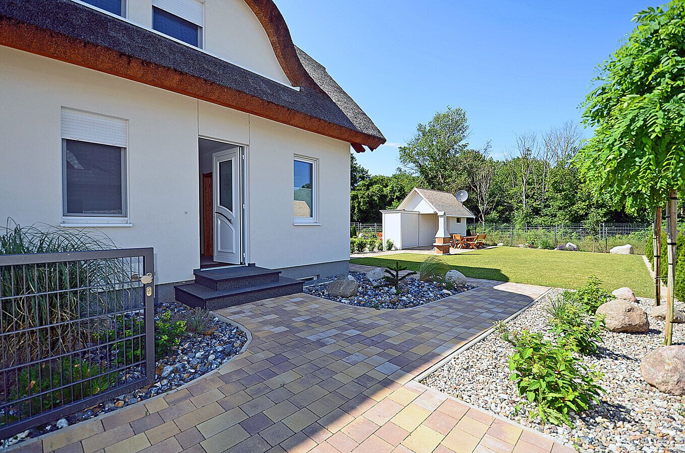 A modern house with a well-maintained lawn, a small shed, and a paved driveway leading to the entrance.