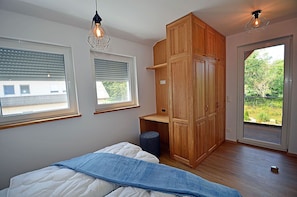 Ein Schlafzimmer mit einem Bett, zwei Fenstern, einem Kleiderschrank und einer Tür, die auf einen Balkon führt.