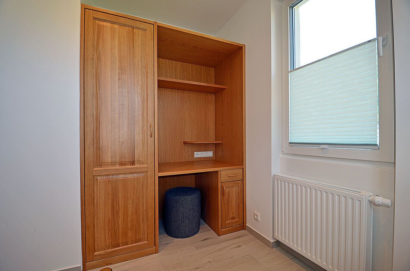 Una habitación con un armario de madera, un radiador y una ventana con persianas.