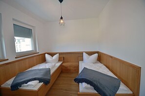 Quarto pequeno e compacto com duas beliches de madeira, uma janela com persianas e um pendente.