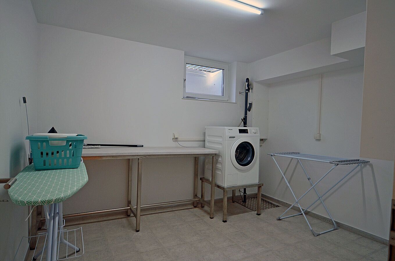 A laundry room with a washing machine, a drying rack, and a small table with a basket.