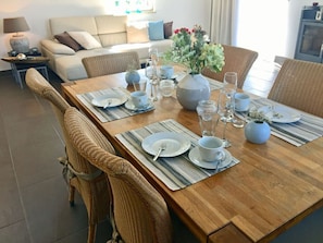 Een eettafel gedekt met borden, bekers en een bloevas, omringd door rieten stoelen.