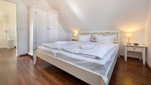 Ein Zimmer mit einem Einzelbett, schrägem Dach, weißer Bettwäsche, einem Kleiderschrank, Nachttischlampen und einem kleinen Tisch.