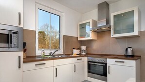 Eine moderne Küche mit weißen Schränken, einem Edelstahlbackofen, einer Mikrowelle und einem Fenster für natürliches Licht.