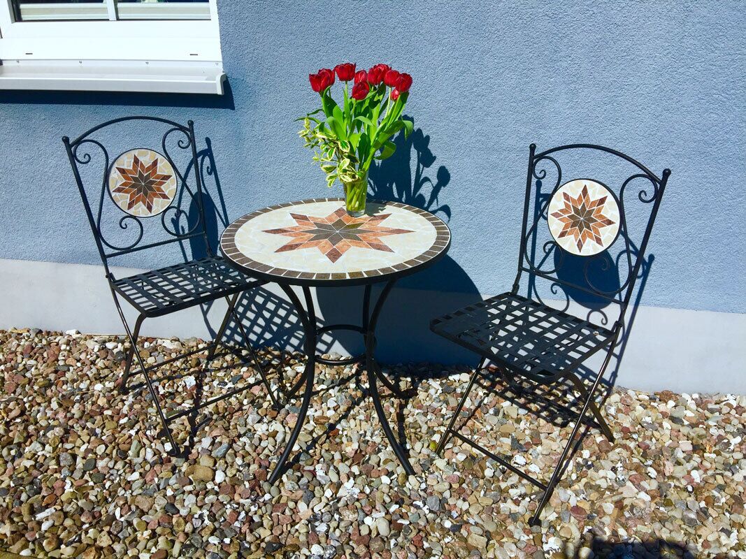 A round table with a star-patterned tile top, flanked by two chairs with decorative backs.