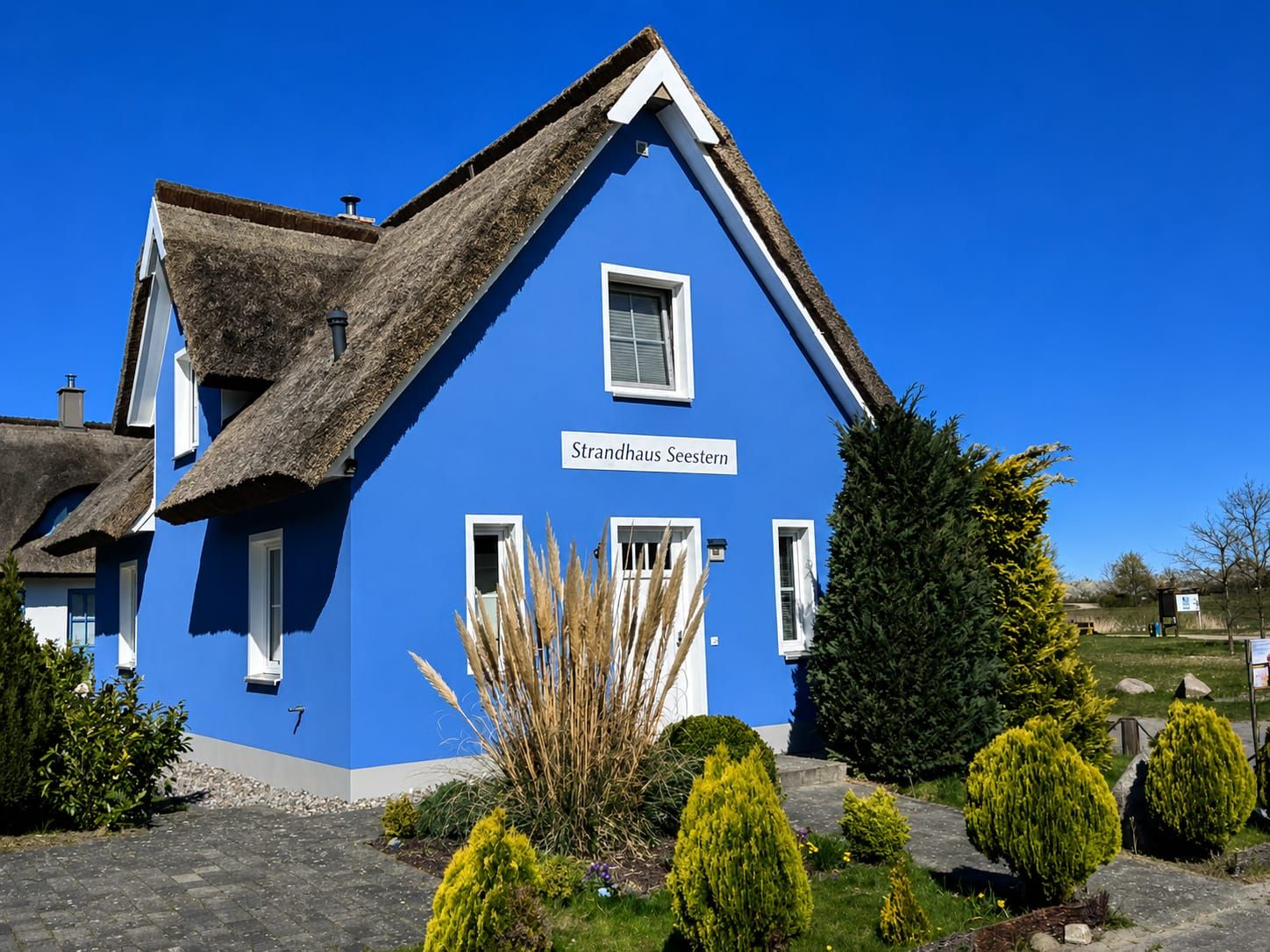 Une maison bleue avec un toit de chaume et une enseigne indiquant « Strandhaus Seestern ».